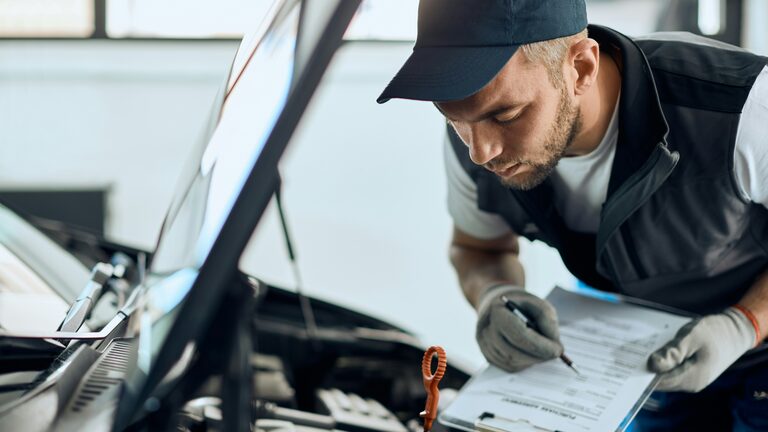 Prüfer begutachtet den Motor eines Fahrzeugs und notiert die Bewertung auf einem Formular