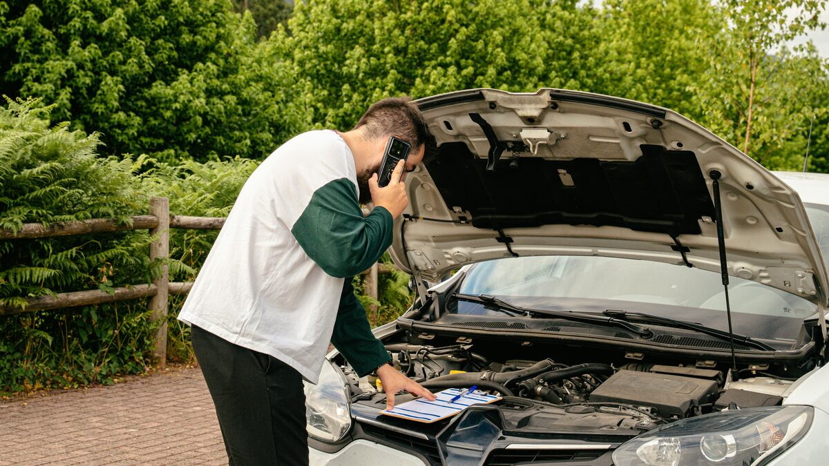 Autofahrer telefoniert vor der geöffneten Motorhaube seines liegengebliebenen Wagens