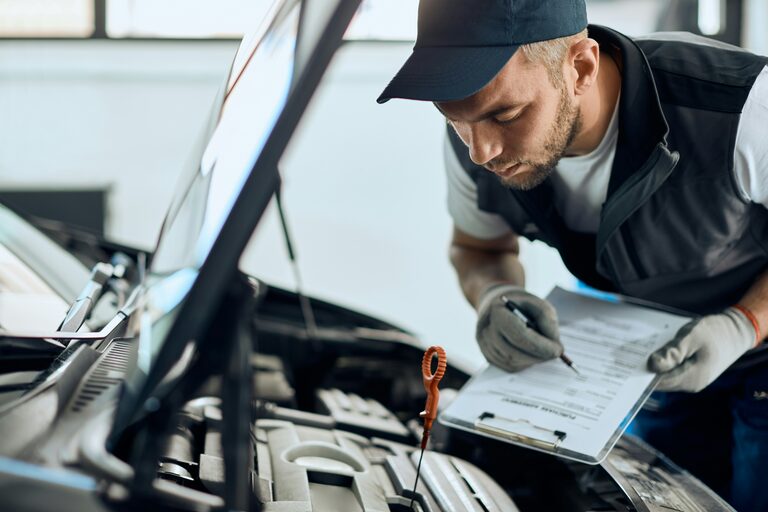 Kfz-Mechaniker prüft den Motor und notiert den Befund auf einem Klemmbrett