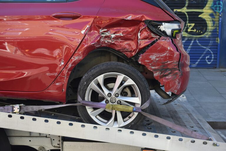 Roter Unfallwagen mit schwerem Heckschaden wird auf einen Abschleppwagen verladen