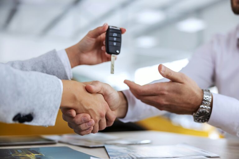 Handschlag über den Kaufunterlagen, dabei wird der Autoschlüssel übergeben